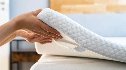 primo piano mani che sollevano un topper per materasso